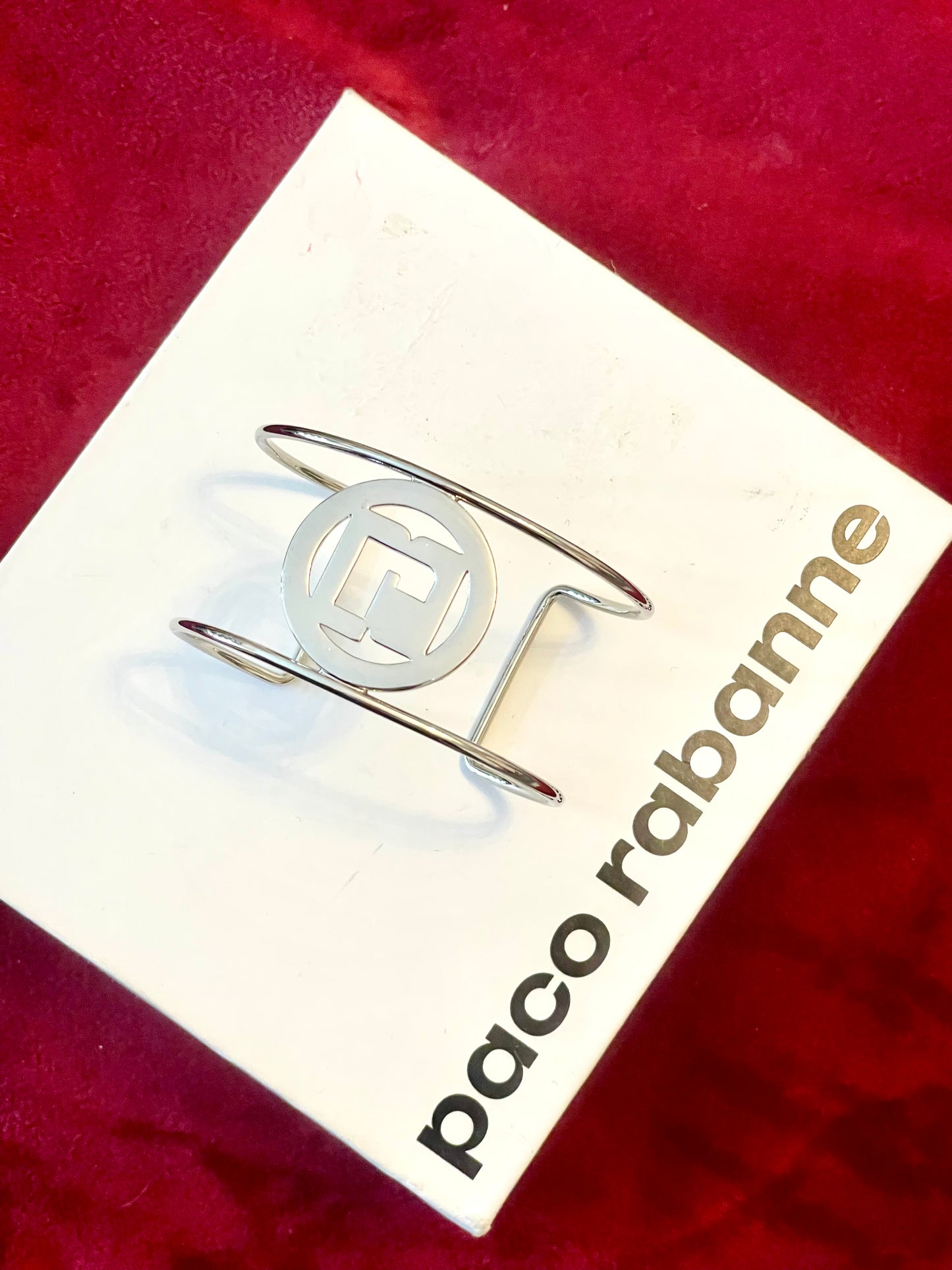 Minimalist vintage Paco Rabanne logo cuff bracelet silver tone On white and red background 