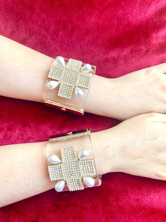 Two transparent plexi bracelets with rhinestone cross designs and faux pearl accents worn on wrists, displayed against a red velvet background. Yves Saint Laurent style Christian Lacroix , Chanel design 