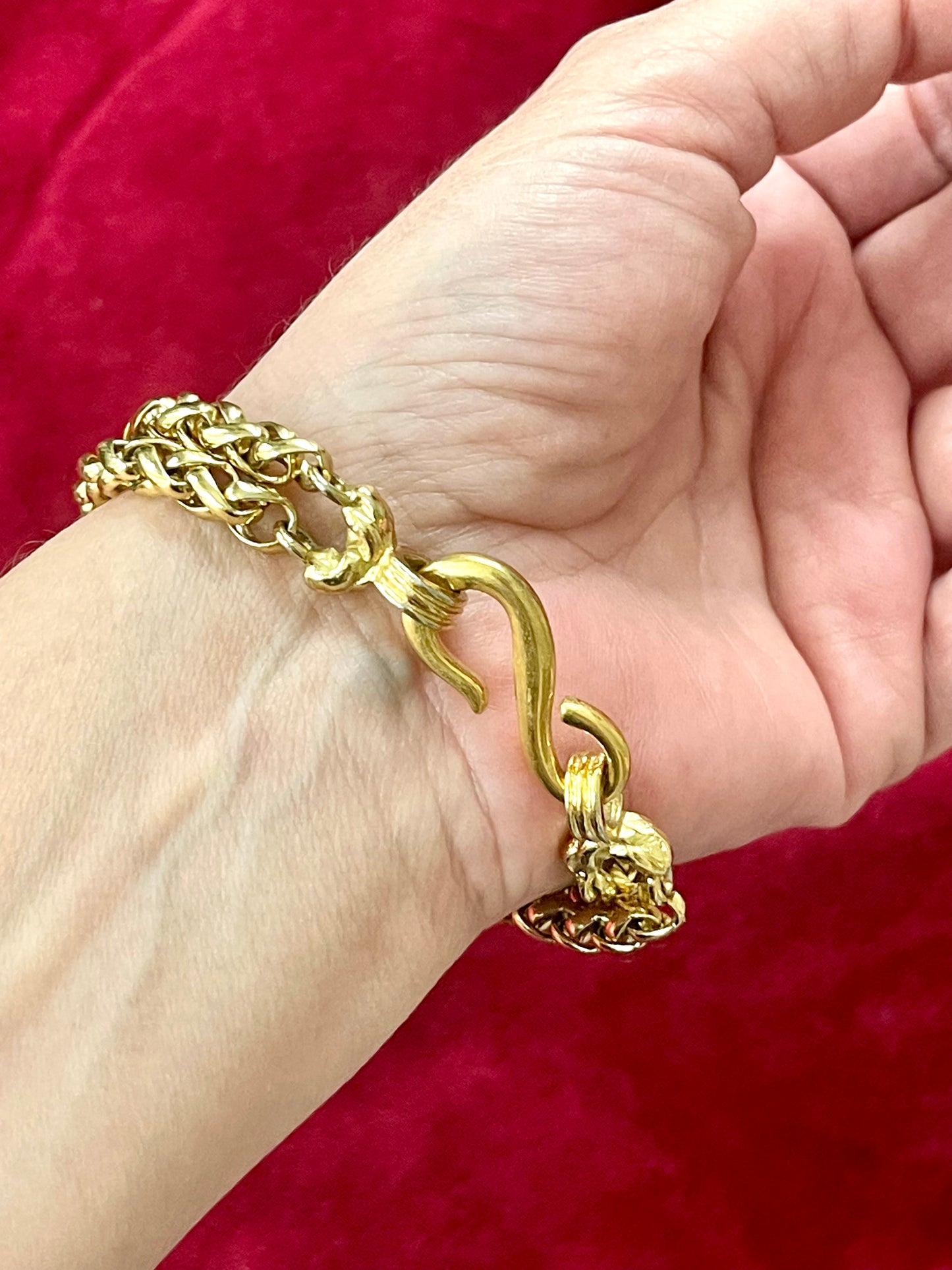 Yves Saint Laurent vintage gold bracelet with a unique clasp on a hand against a red background
