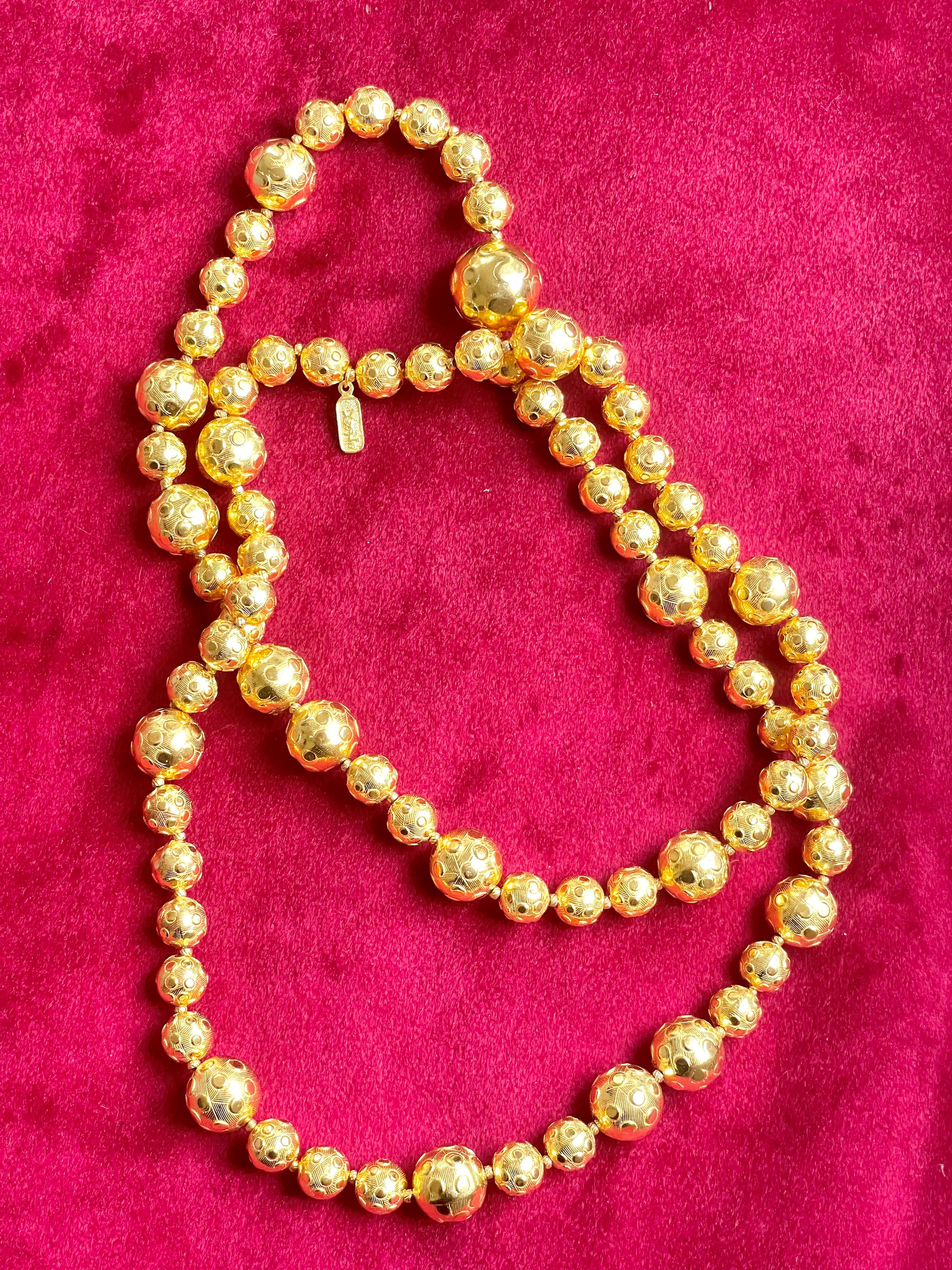 Vintage Yves Saint Laurent gold beaded necklace with textured graduated beads displayed on red velvet background showing tag