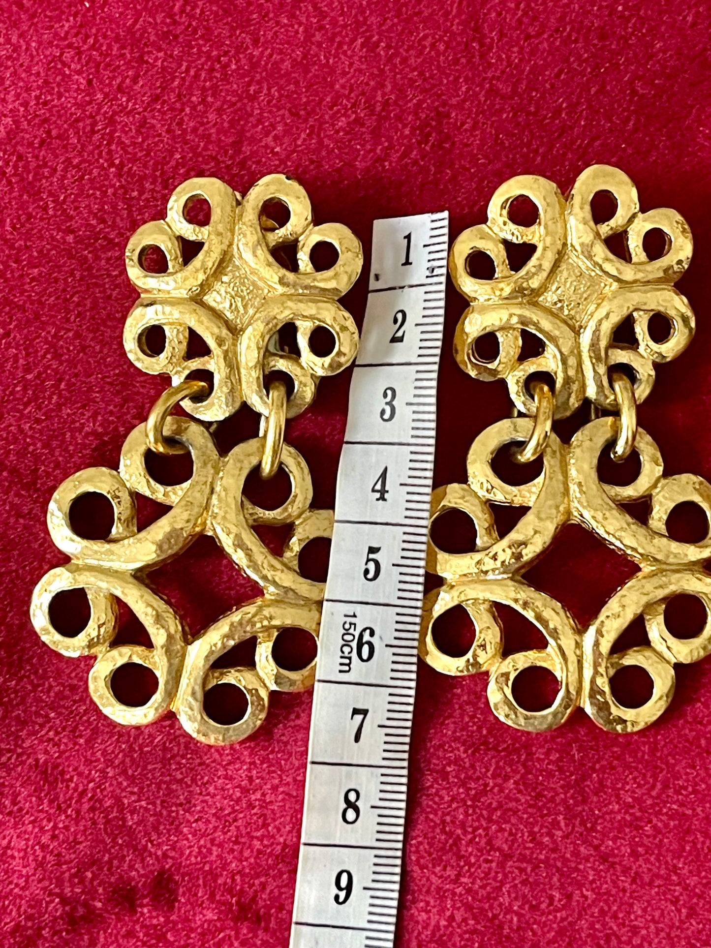 Front view of vintage gold-tone Yves Saint Laurent statement drop earrings displayed on a red background, with a measuring tape showing approximately 8 cm length