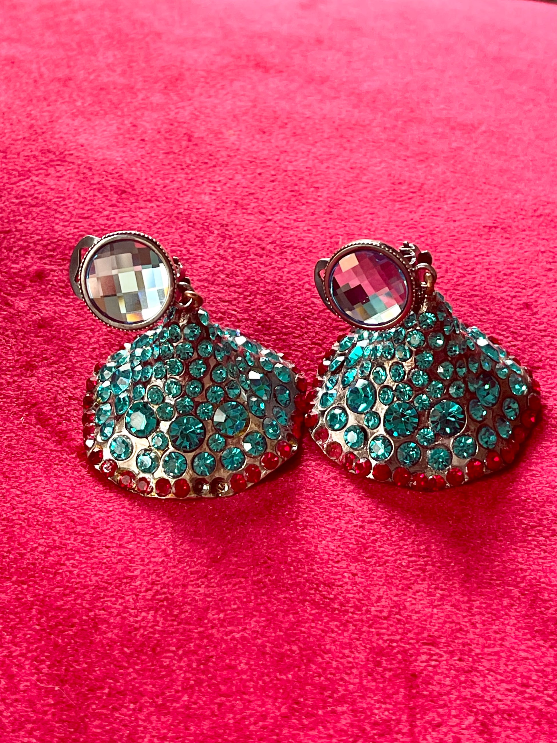 Close-up of Yves Saint Laurent Rive Gauche vintage statement earrings with turquoise and red rhinestones against a red velvet background.