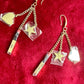 Close up view of Front view of Yves Saint Laurent Beauté upcycled earrings with lipstick, star, and heart charms on gold-plated hoops on red background 