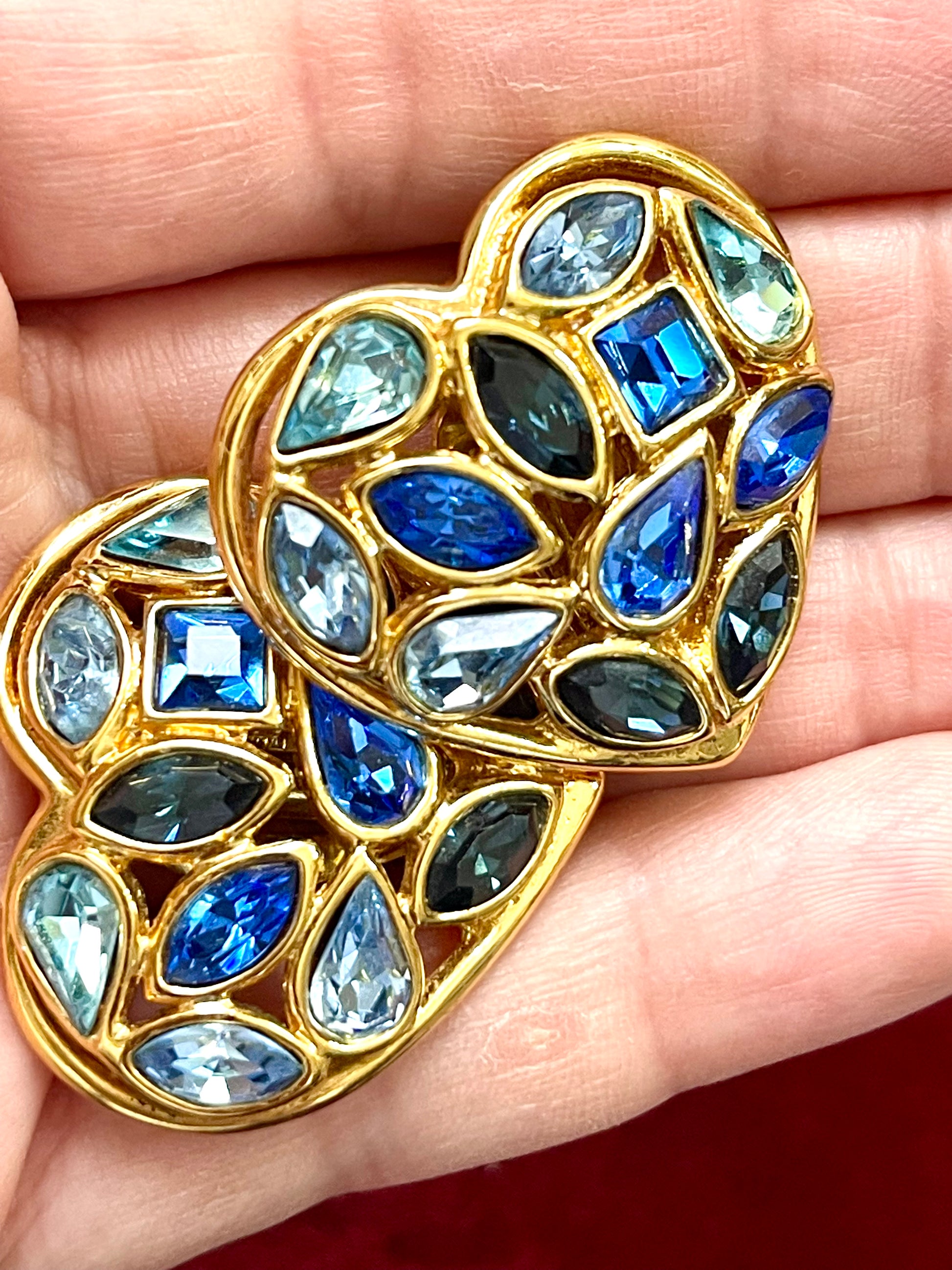 Close up of gold-tone vintage Yves Saint Laurent heart-shaped clip-on earrings decorated with multi-coloured crystals, displayed on a hand