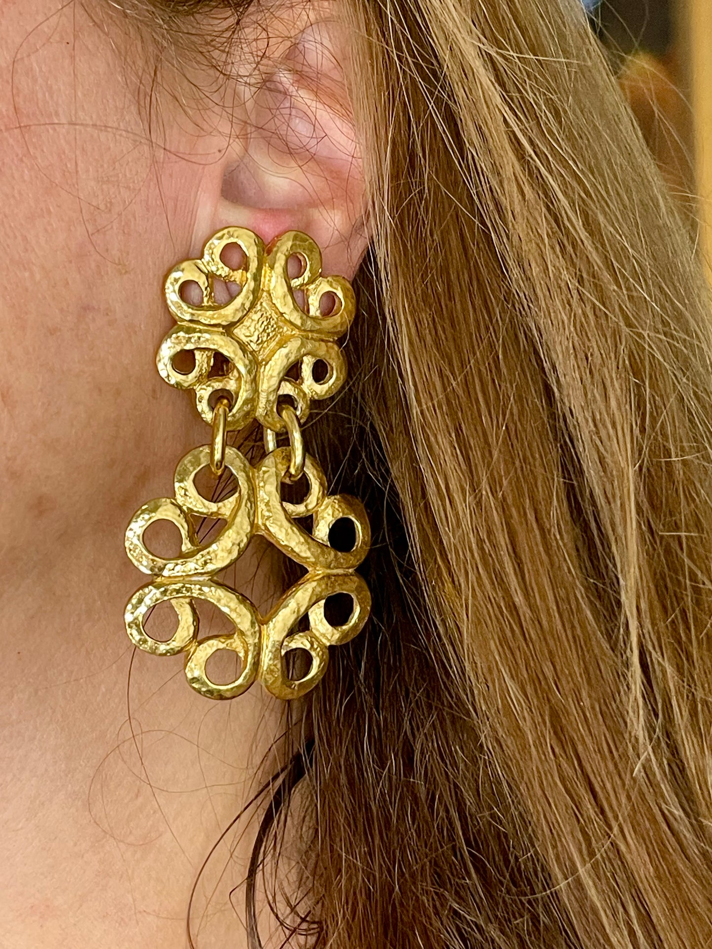 Model wearing vintage gold-tone Yves Saint Laurent statement drop earrings displayed on a red background 