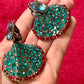 Close-up of Yves Saint Laurent Rive Gauche vintage statement earrings with turquoise and red rhinestones held in hand against a red velvet background.