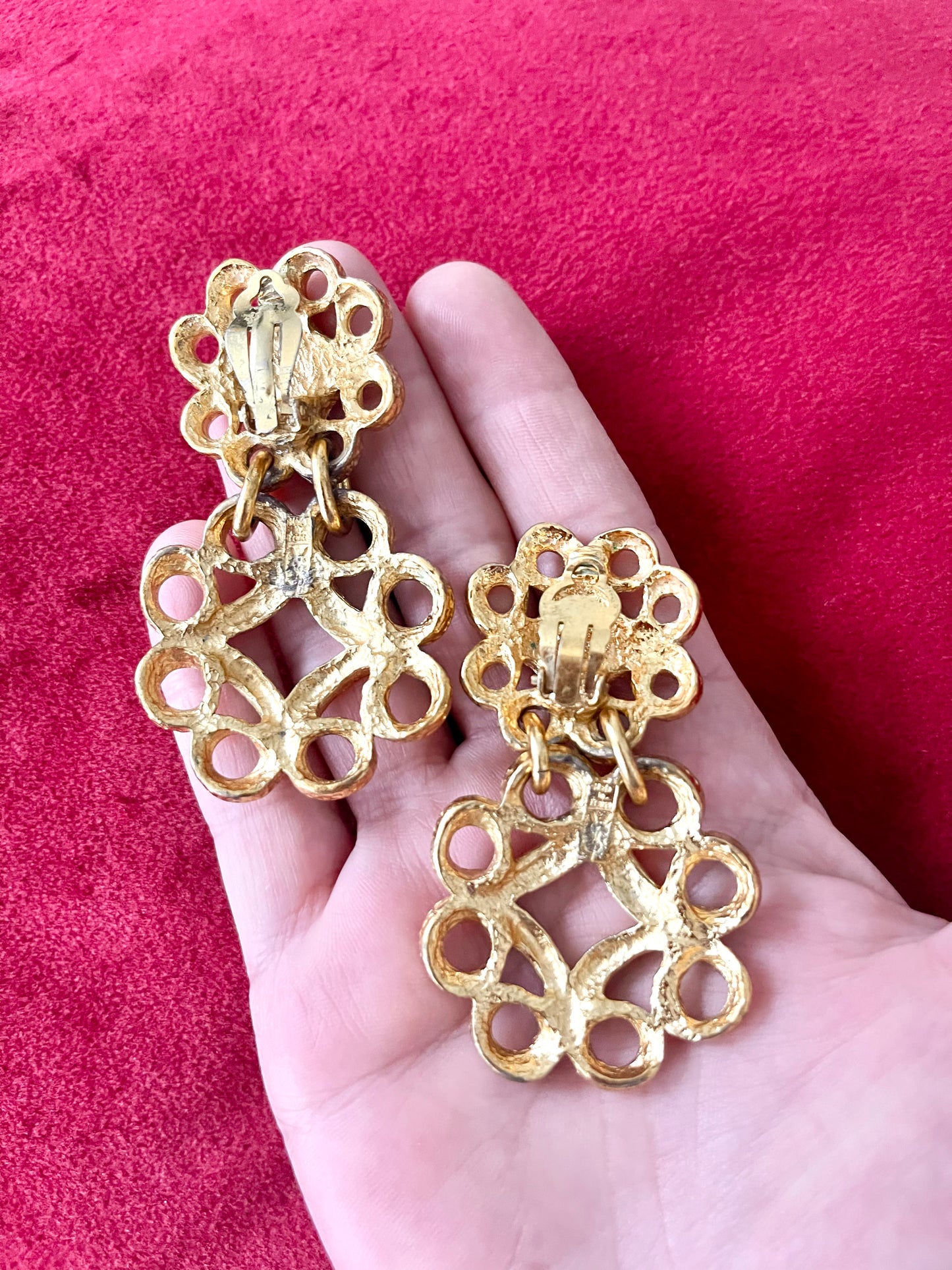 Back view of vintage YSL gold-tone earrings showing textured metal, clip-on closure, and the YSL signature mark on the lower segment Displayed on hand with a red background 