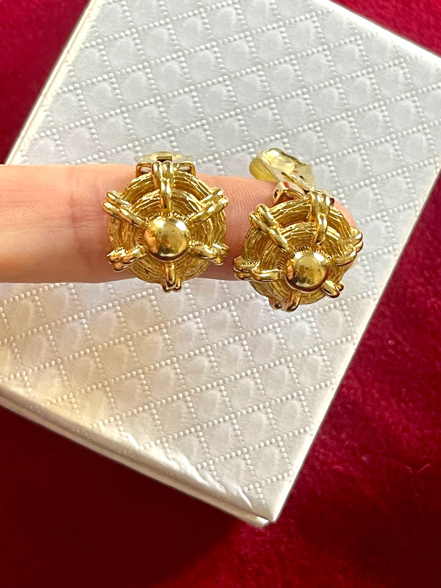 Vintage Christian Dior gold tone earrings held between fingers against a white box background