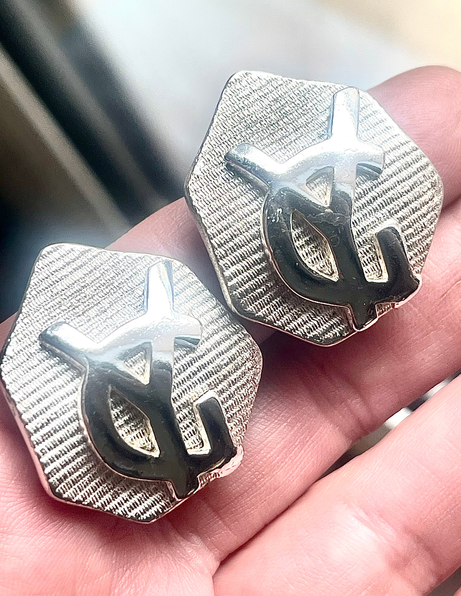 Close-up of vintage YSL silver-tone hexagon earrings resting on the hand, showing the textured surface and raised YSL monogram.