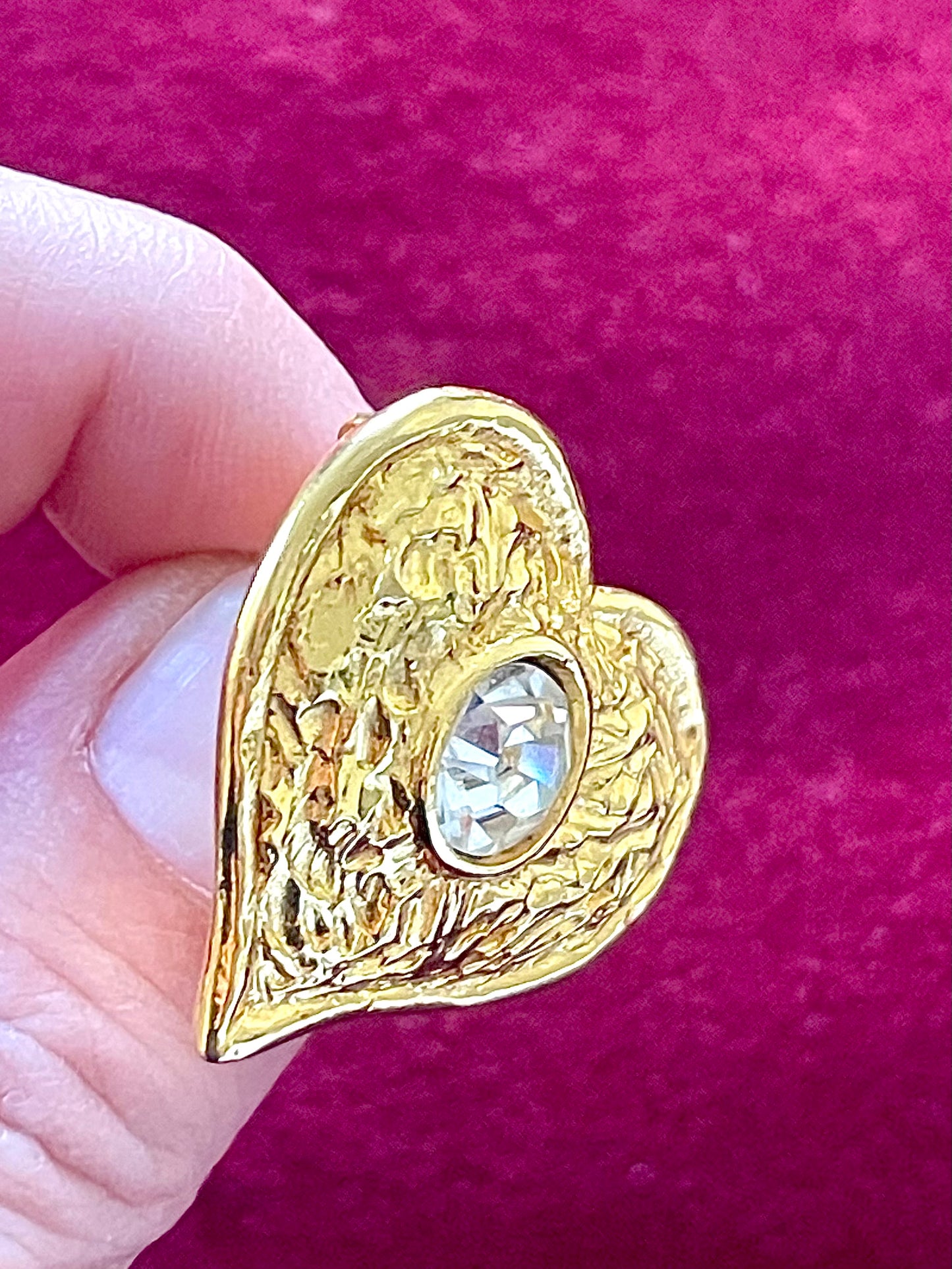 Side angle of gold-tone wave motif on Rambaud brooch held by hand with a red background 