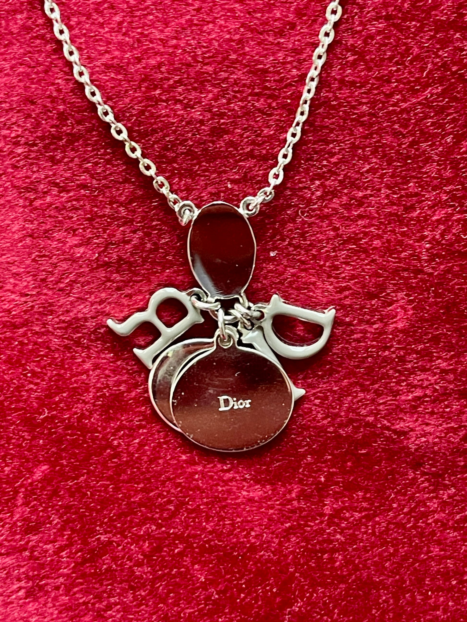 Close up Backside view of the Dior necklace showing the reverse of the letter charms and chain on red velvet fabric.