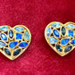 Pair of 3 cm gold-tone vintage Yves Saint Laurent heart-shaped clip-on earrings decorated with multi-coloured crystals, displayed on a red background