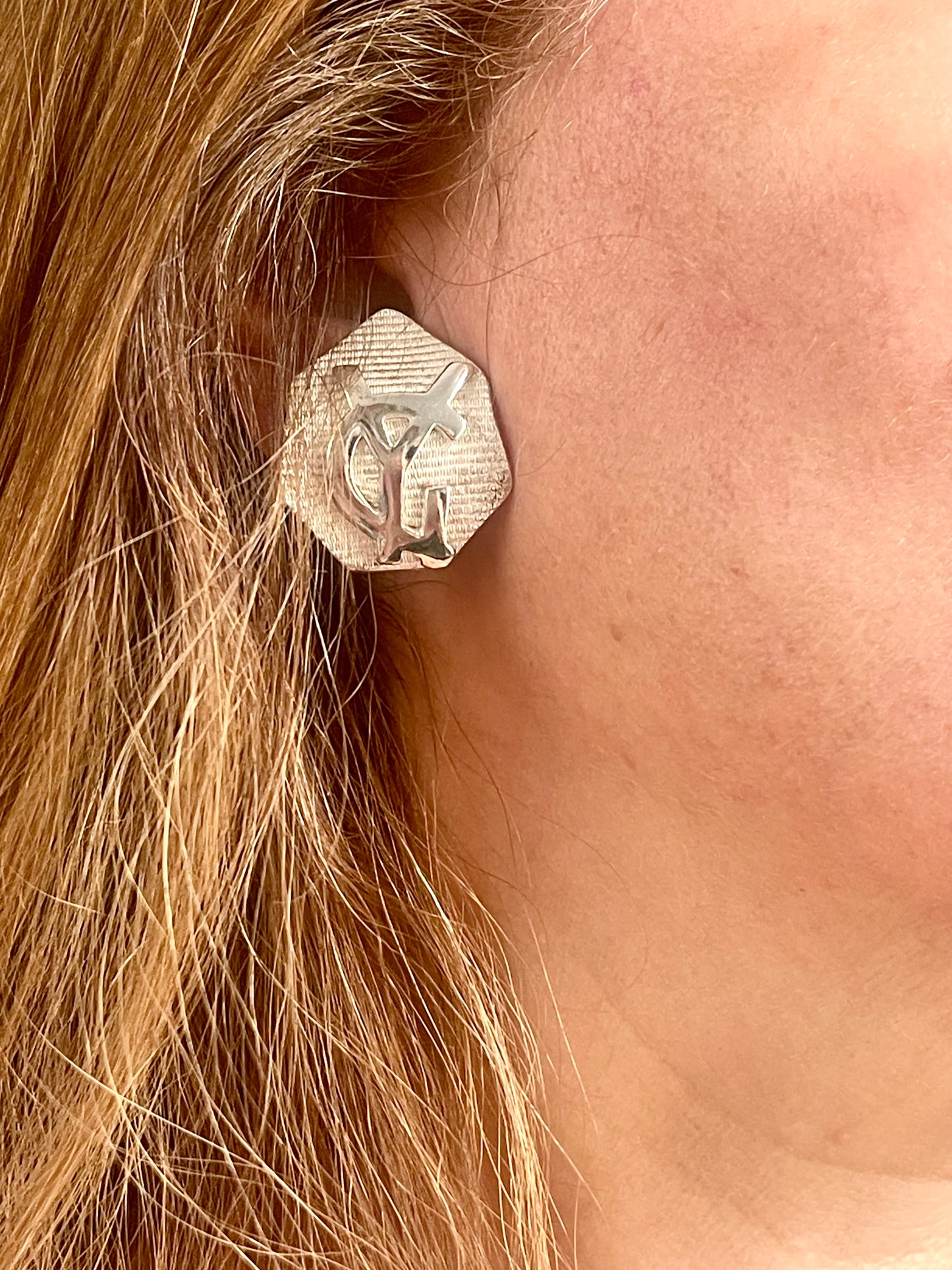 Worn by model Close-up of vintage YSL silver-tone hexagon earrings resting on the hand, showing the textured surface and raised YSL monogram.