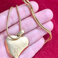 Gold heart-shaped YSL pendant on a chain held in a hand against a red background showing backside signature 