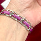 Dior Silver chain bracelet with purple braided cord on a wrist against a red background