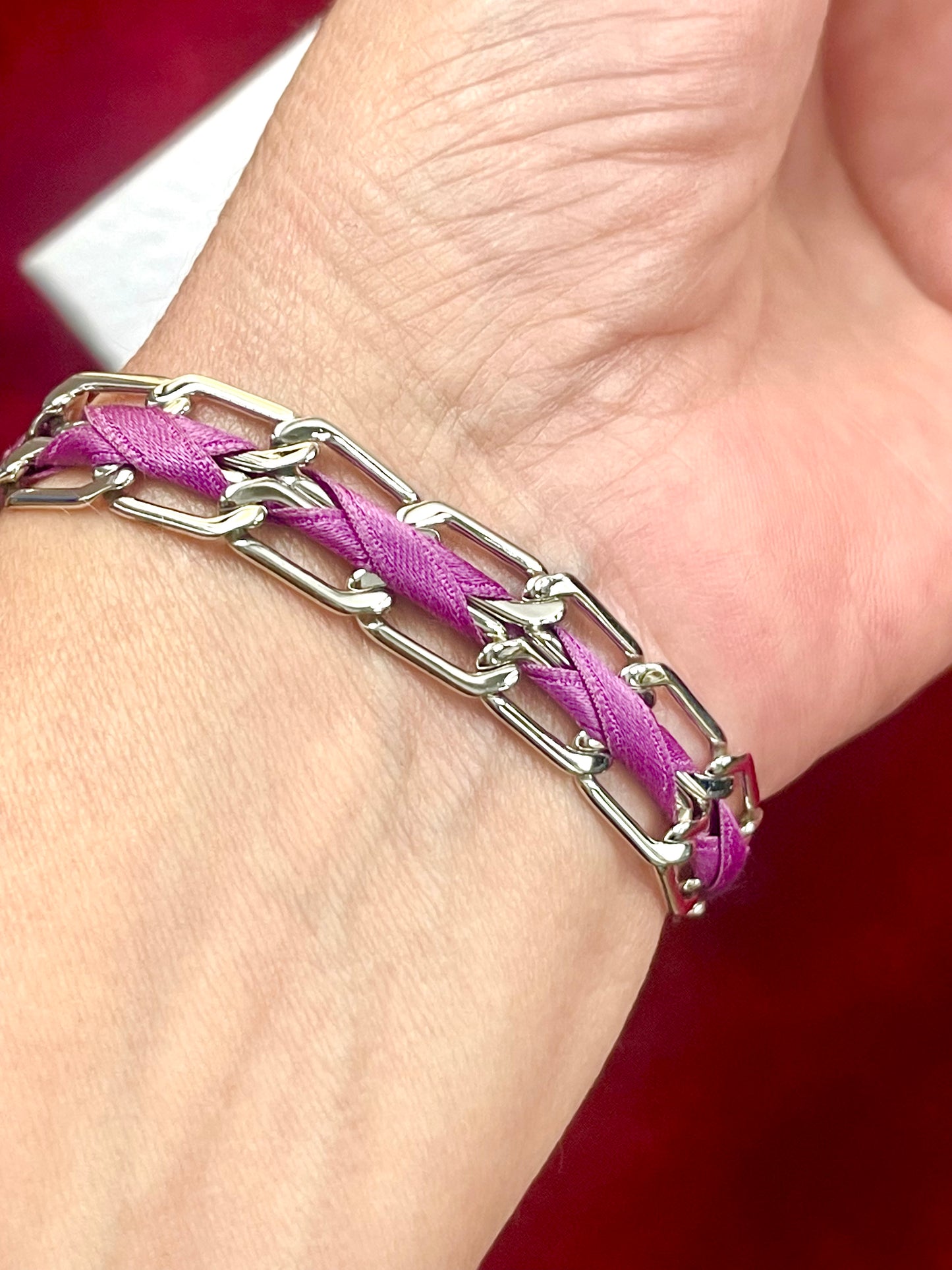 Dior Silver chain bracelet with purple braided cord on a wrist against a red background