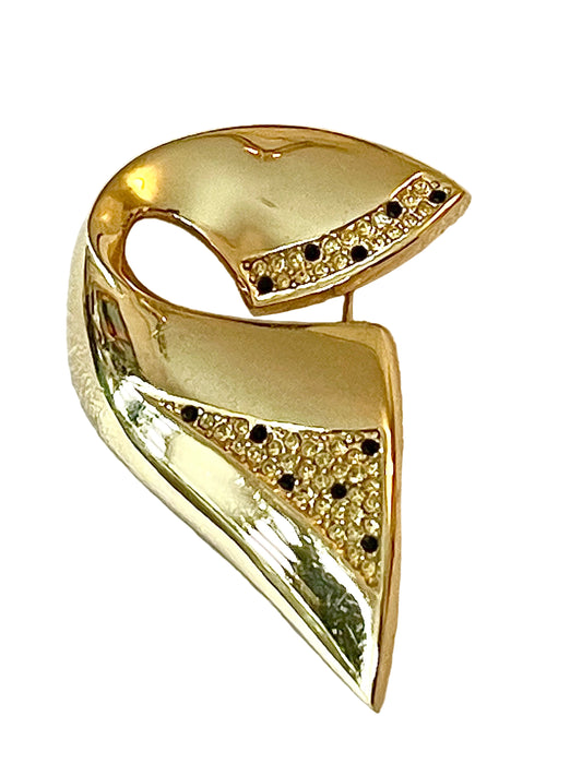 Vintage Christian Dior gold-tone sculptural brooch decorated with black and clear rhinestones, displayed against a white background