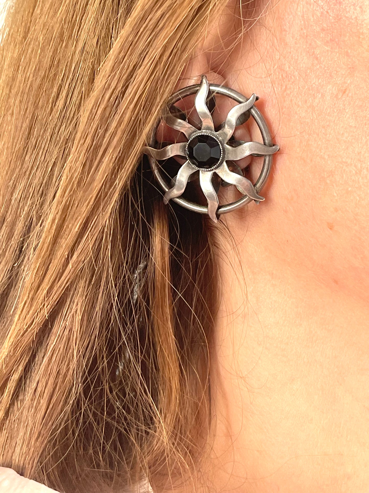 Model wearing 1980s Paco Rabanne silver-tone sun earrings with dark faceted center stones, highlighting detailing and condition.