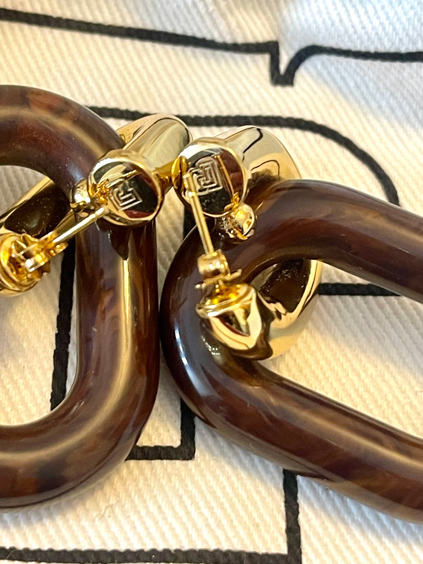 Close up on butterfly clasp detail on Paco Rabanne XL Link earrings, brown resin and gold metal, made in Italy On red background 