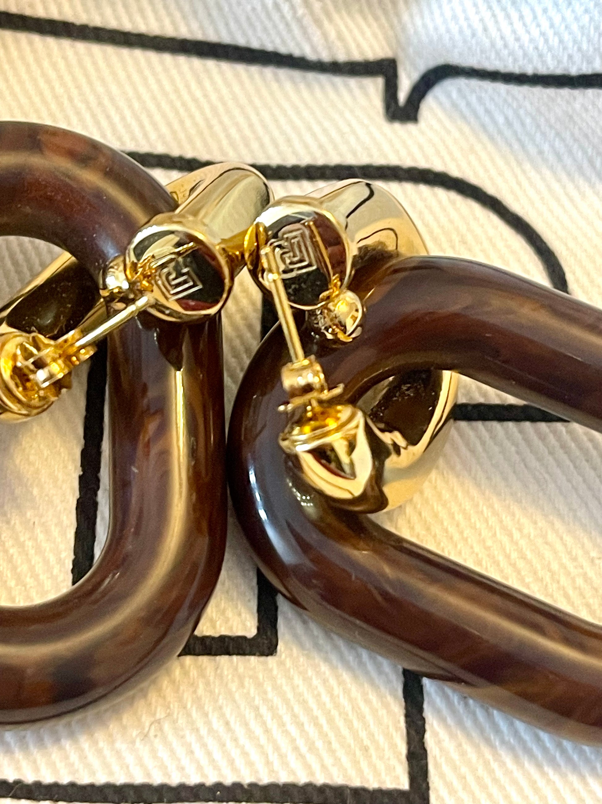 Close up on butterfly clasp detail on Paco Rabanne XL Link earrings, brown resin and gold metal, made in Italy On red background 