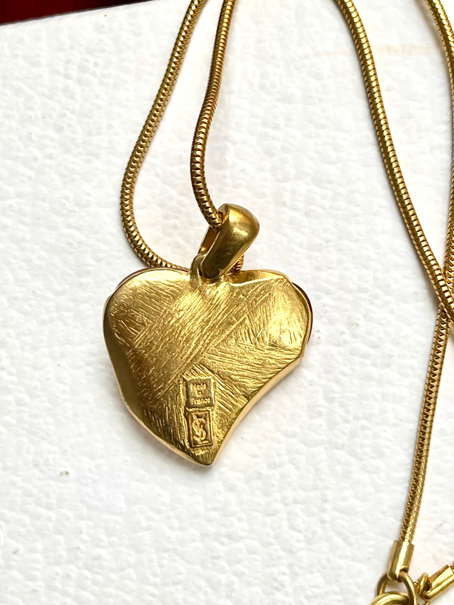 Gold heart-shaped Yves Saint Laurent pendant on a chain against a white background