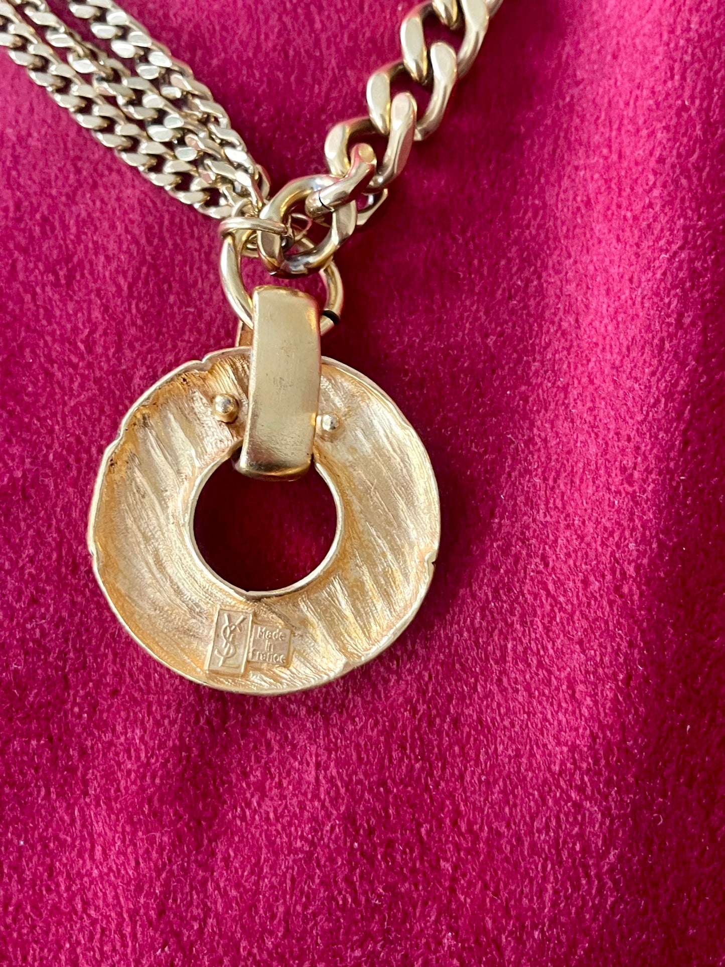 Backside view of Yves Saint Laurent vintage 80s pendant  showing hallmark signature YSL made in France on red background 