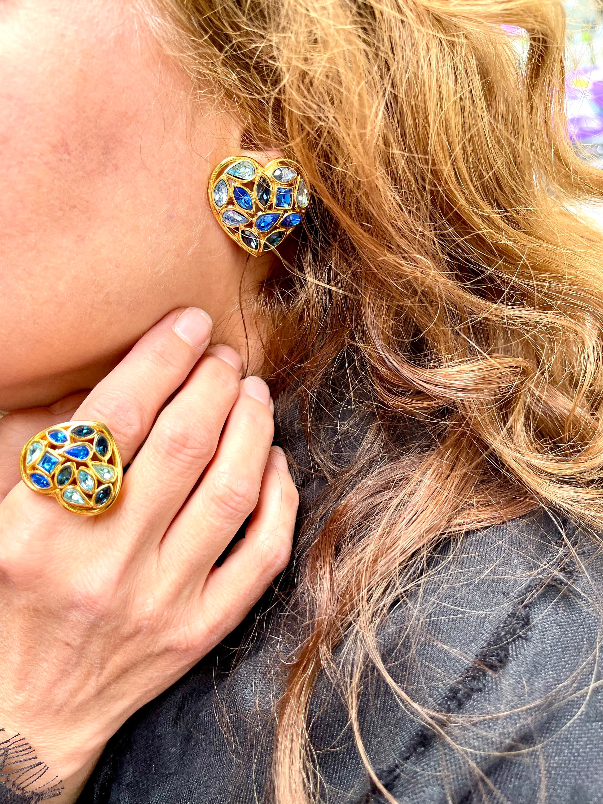 Close-up of a person wearing a gold and blue heart-shaped earring and ring vintage Yves Saint Laurent 