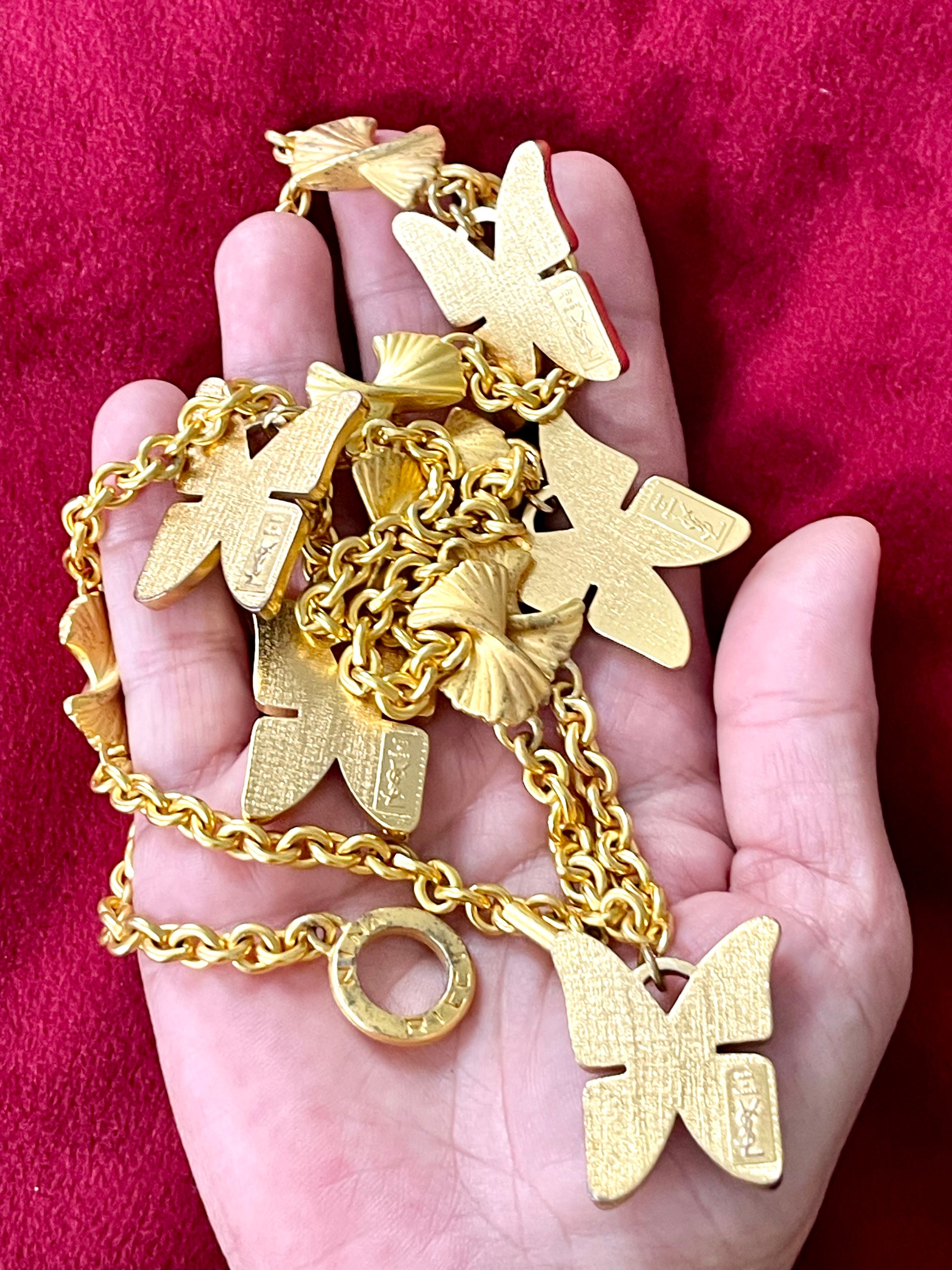 Back side view of Vintage 80s five Yves Saint Laurent Butterfly Enameled pendants mounted on a Nina Ricci gold necklace, displayed on hand 