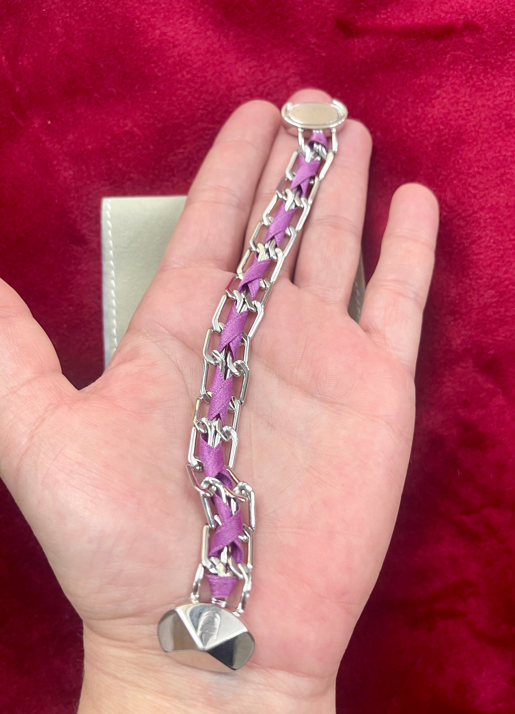 Hand holding Dior vintage bracelet silver tone jewelry flat lay against a red background 