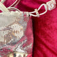 Close up on closing straps of Paco Rabanne silver shoulder/wrist bag with both straps shown, on red velvet fabric background.