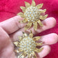 Vintage Yves Saint Laurent Gold sun-shaped earrings with rhinestones held by hand against a pink background