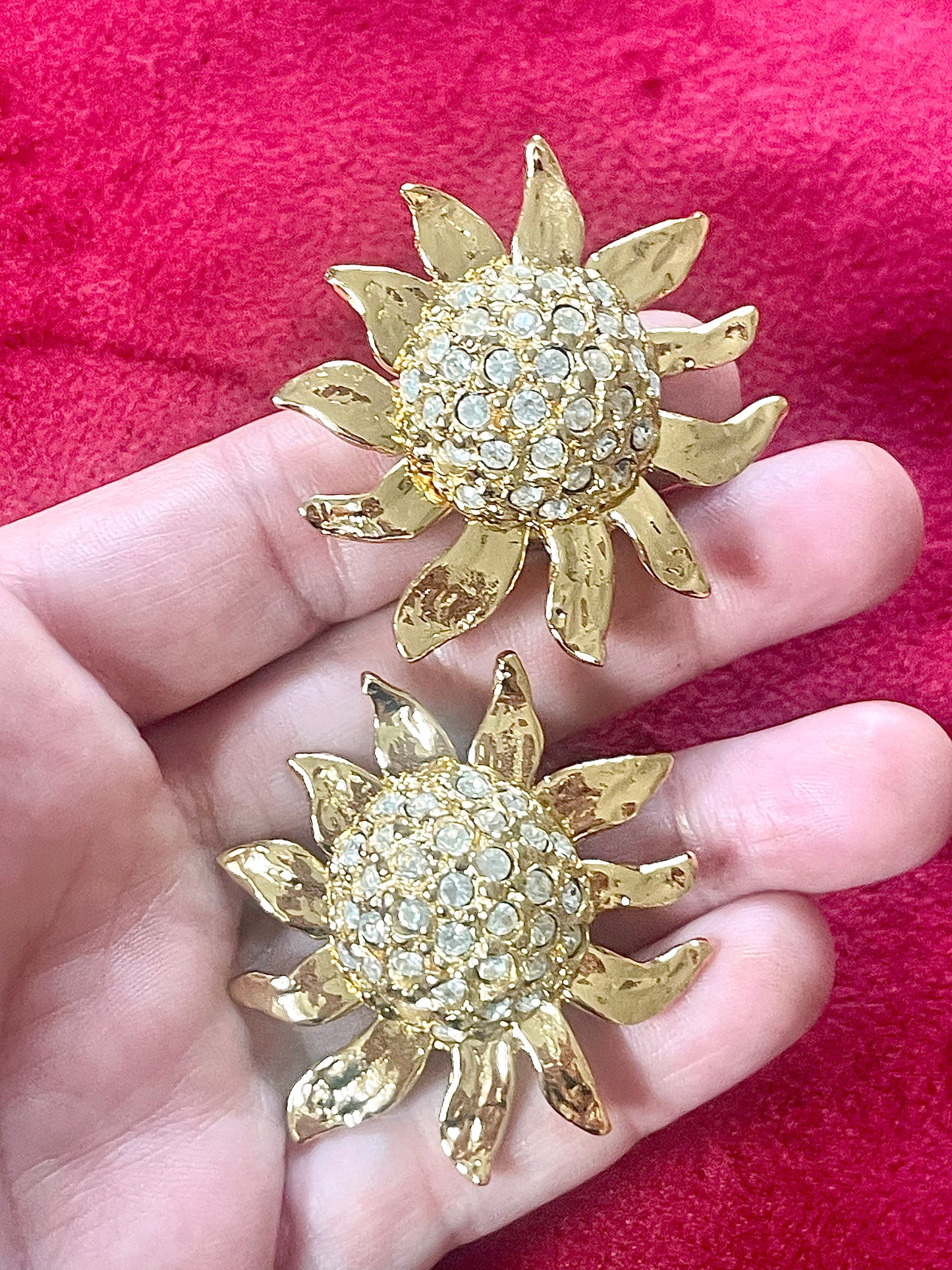 Vintage Yves Saint Laurent Gold sun-shaped earrings with rhinestones held by hand against a pink background