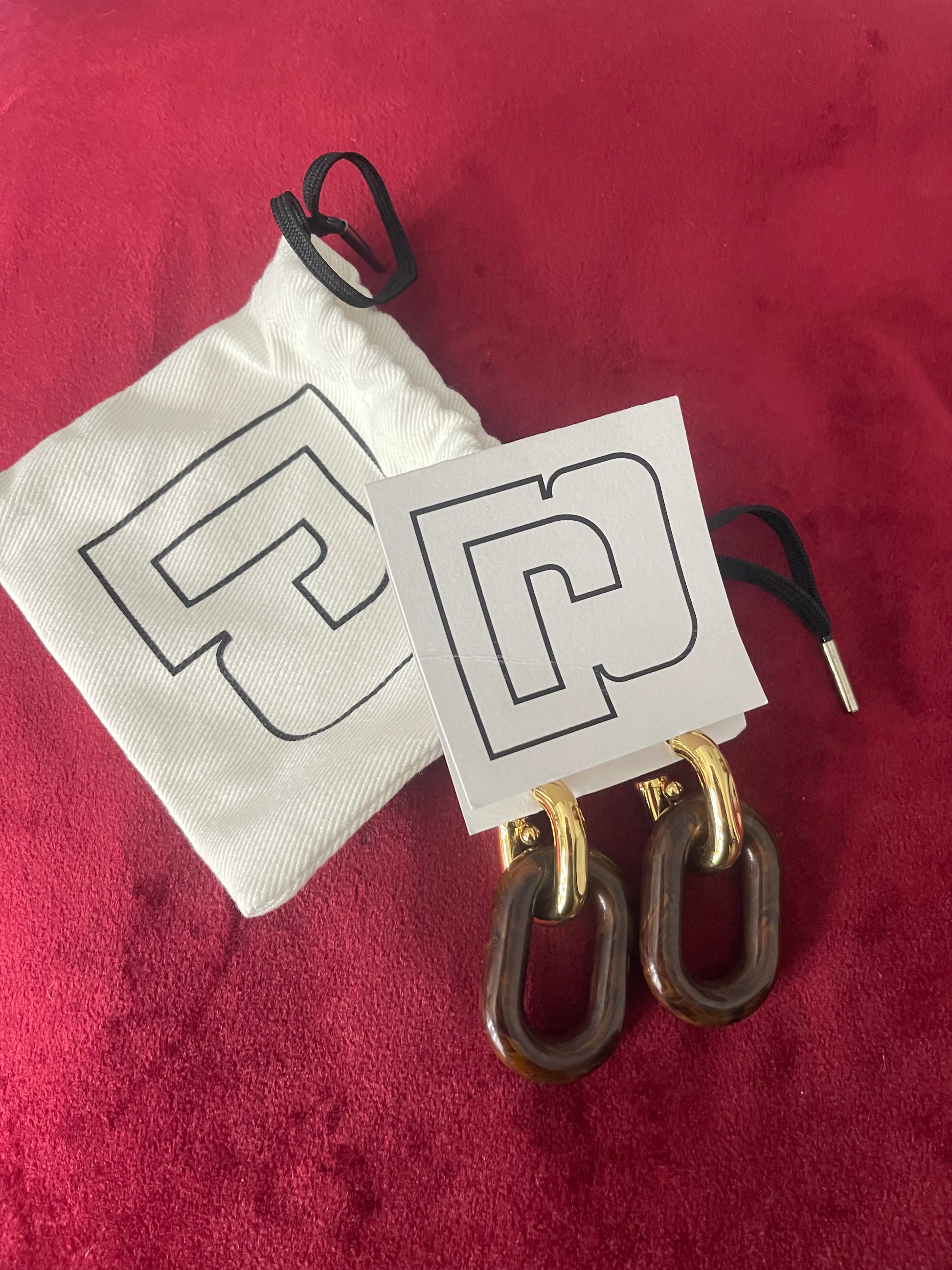 Paco Rabanne XL Link earrings in brown resin and gold metal, front view, 2025 collection, made in Italy Included pouch and tag card on red background 