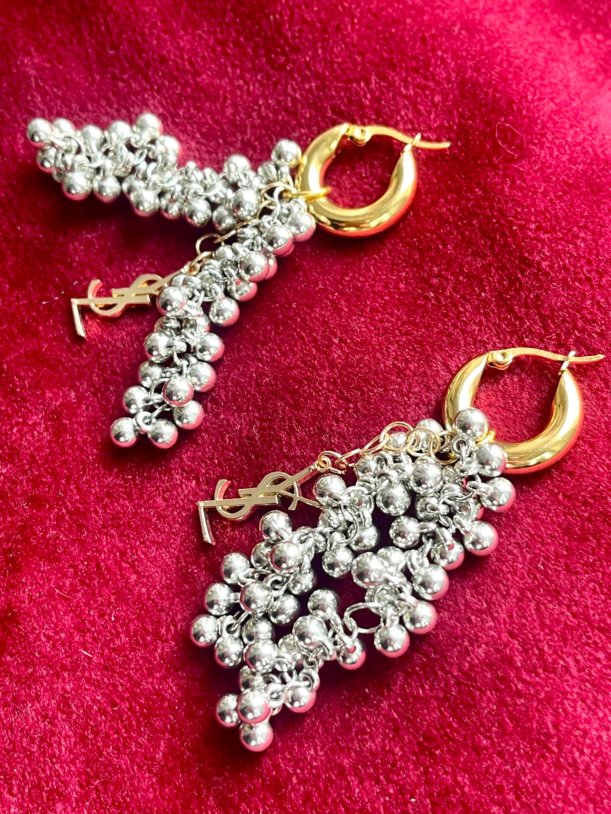 Close up side view of a pair of Gold and silver earrings with pearl-like beads and YSL Yves Saint Laurent charms