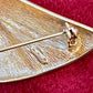 Close up in signature of Vintage Christian Dior gold-tone sculptural brooch decorated with black and clear rhinestones, displayed against a red background