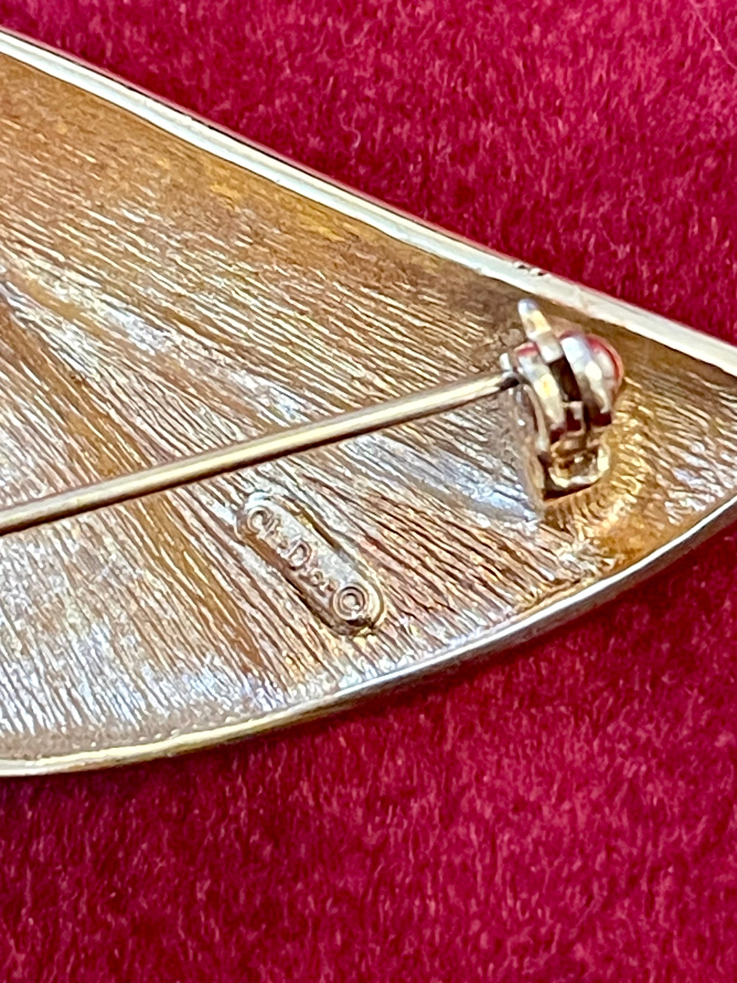 Close up in signature of Vintage Christian Dior gold-tone sculptural brooch decorated with black and clear rhinestones, displayed against a red background