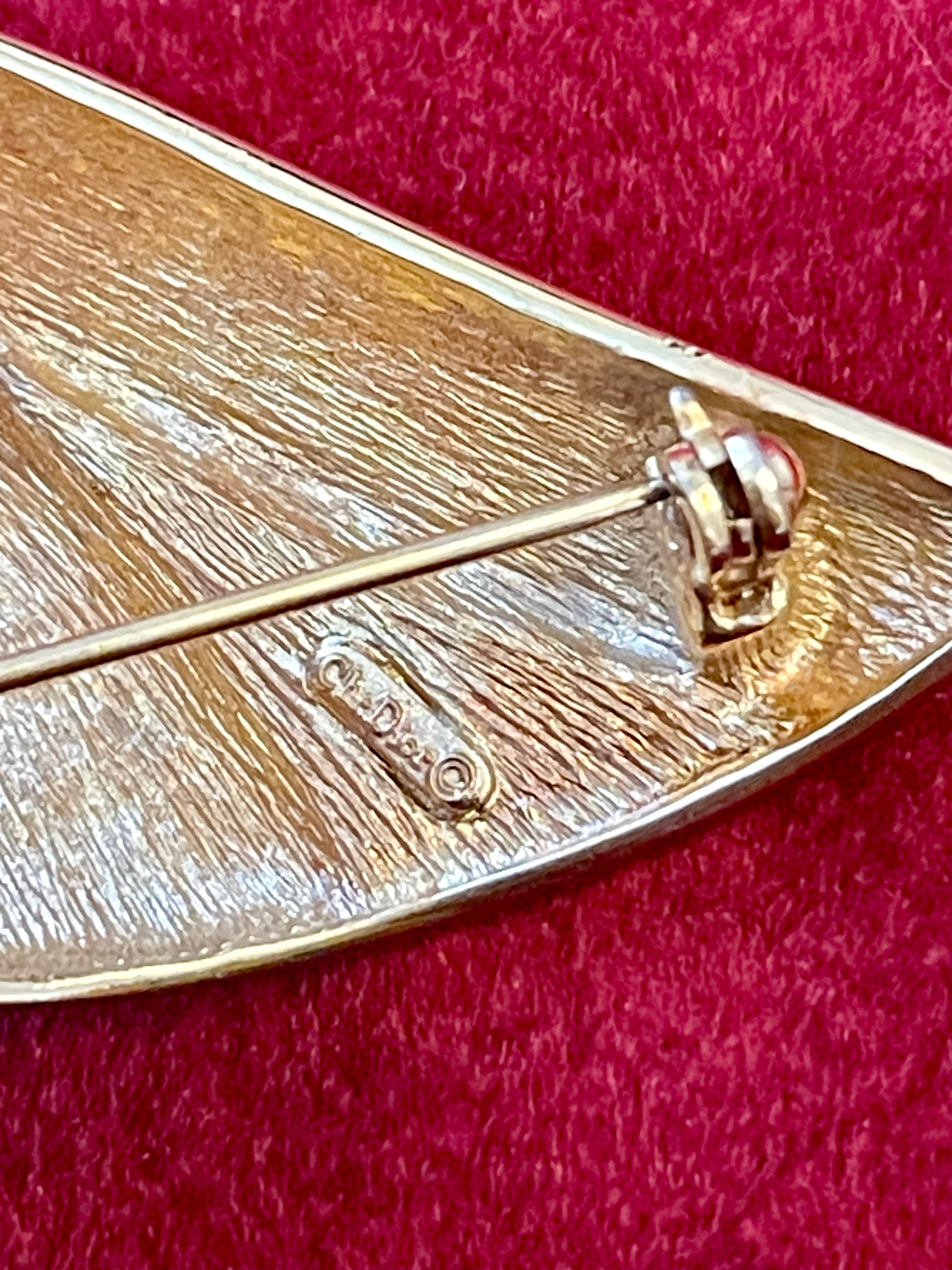 Close up in signature of Vintage Christian Dior gold-tone sculptural brooch decorated with black and clear rhinestones, displayed against a red background