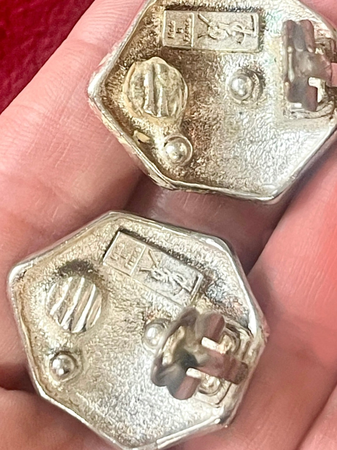 Close up on hallmarks and made in France Close-up of vintage YSL silver-tone hexagon earrings resting on the hand, showing the textured surface and raised YSL monogram. Held by hand 