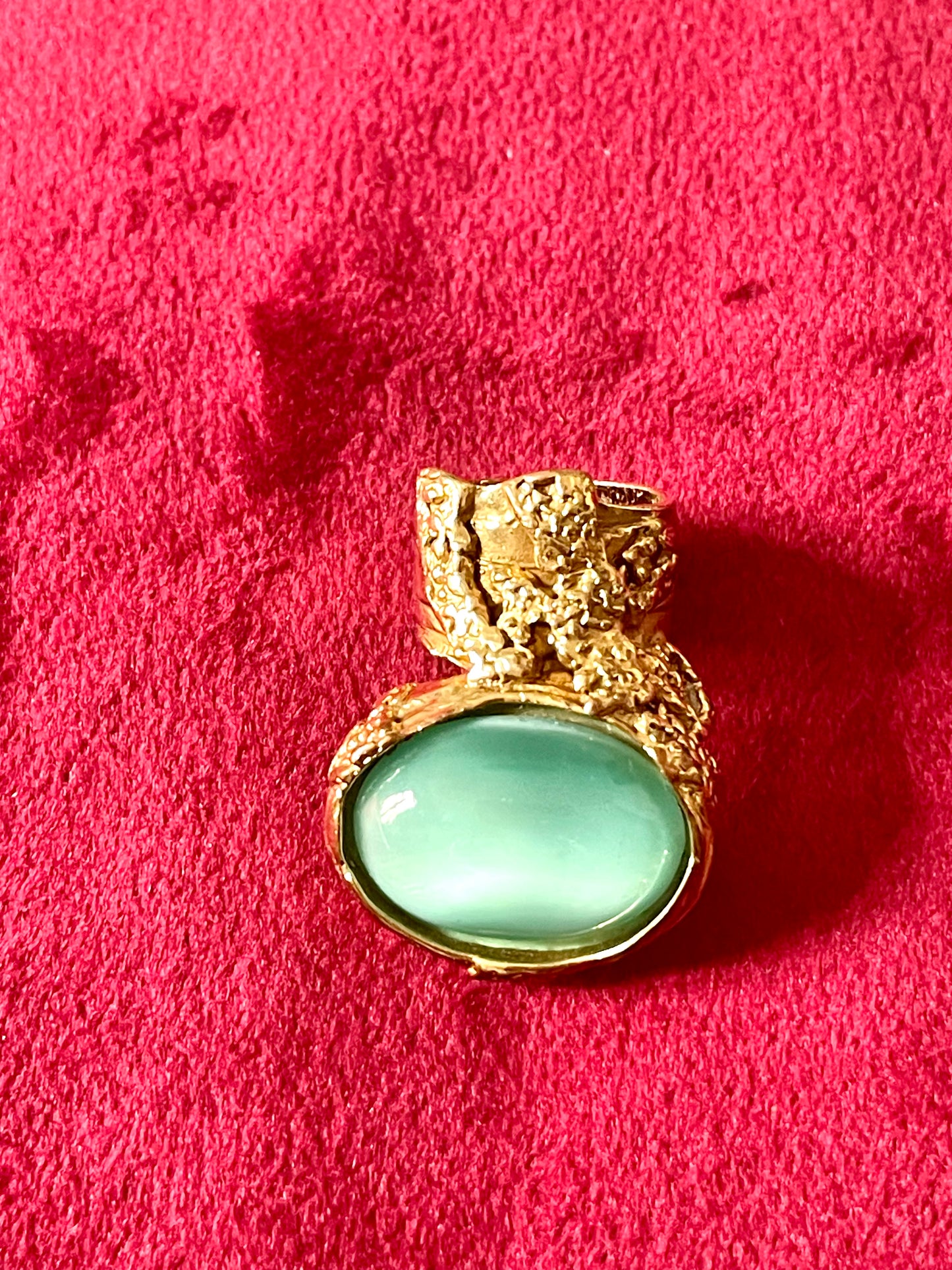 Vintage Yves Saint Laurent ring featuring a large turquoise nacre stone set in sculpted gold metal, displayed on a red velvet surface.