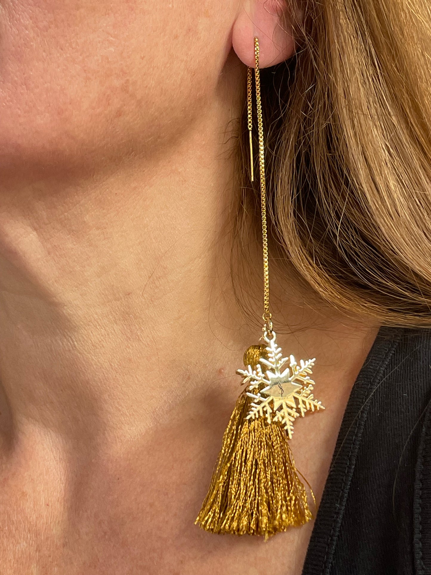 Gold earring with YSL snowflake design and tassel on a person's ear