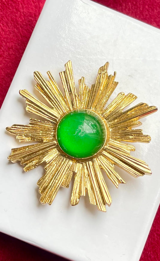 Vintage Yves Saint Laurent 1980s gold-tone sunburst brooch with green cabochon center on white display
