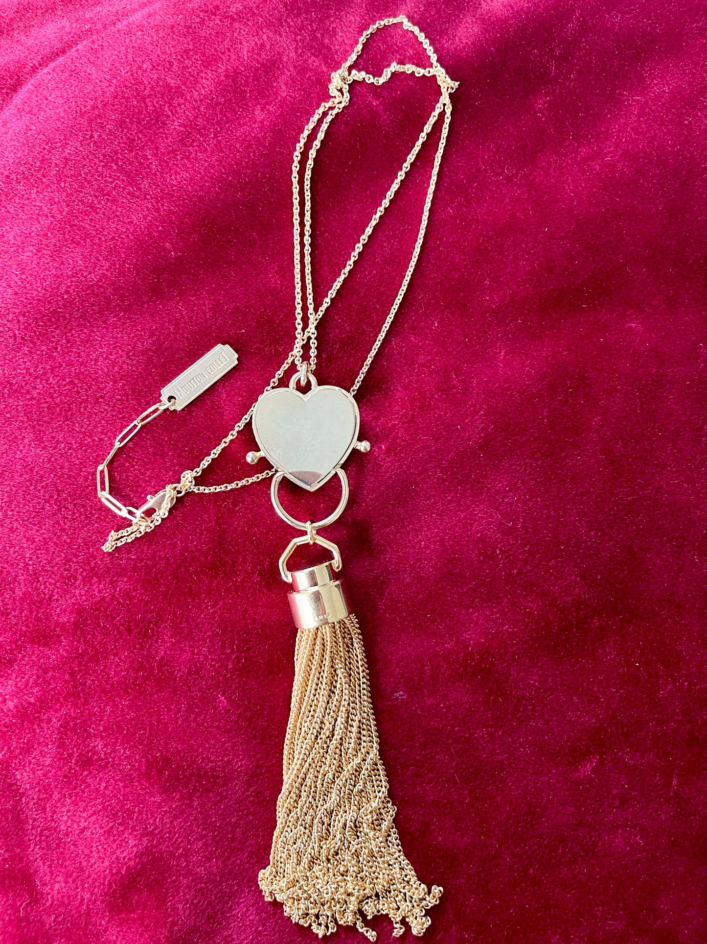 Back view of Gold-plated necklace from Mutton Collet with YSL tassel charm and branded chain tag shown on red velvet fabric