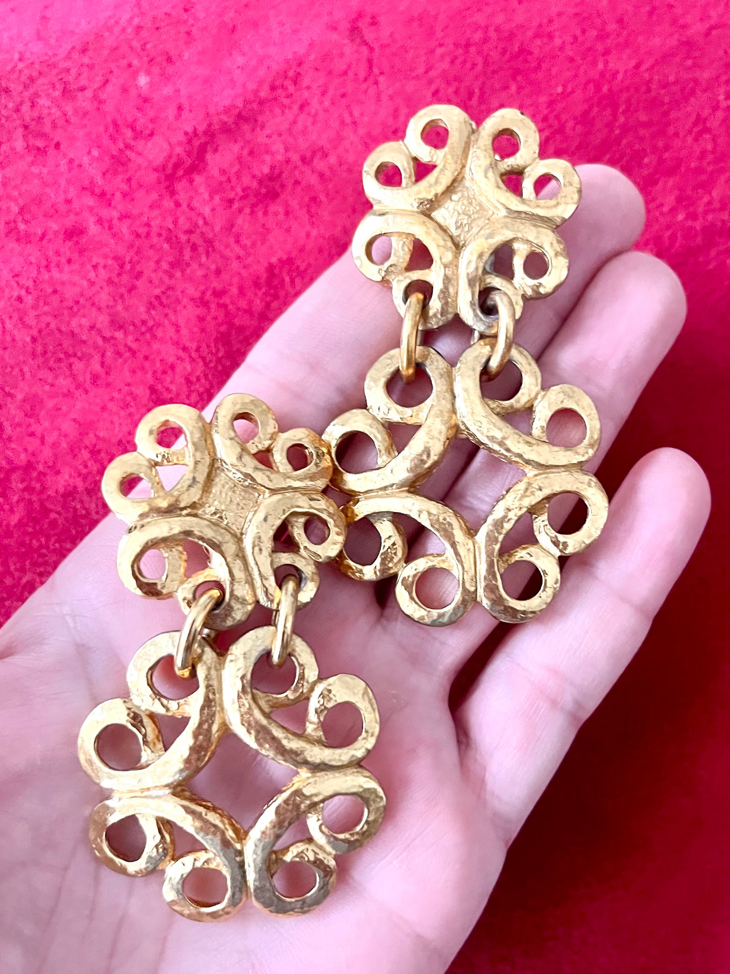 Close up view of vintage gold-tone Yves Saint Laurent statement drop earrings displayed on hand with a  red background,