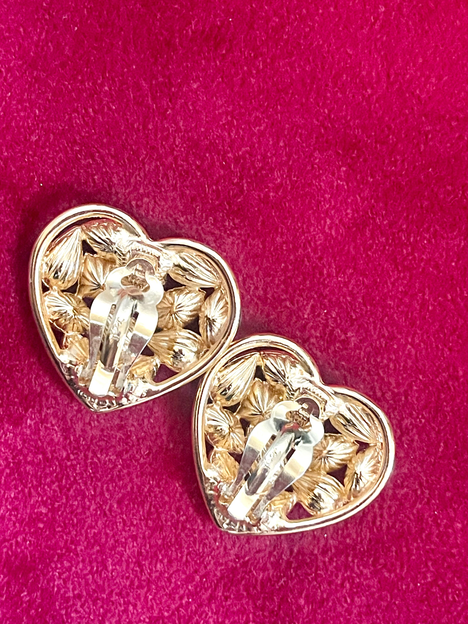 Back view of Pair of 3 cm gold-tone vintage Yves Saint Laurent heart-shaped clip-on earrings decorated with multi-colored crystals, displayed on a red background showing signature 