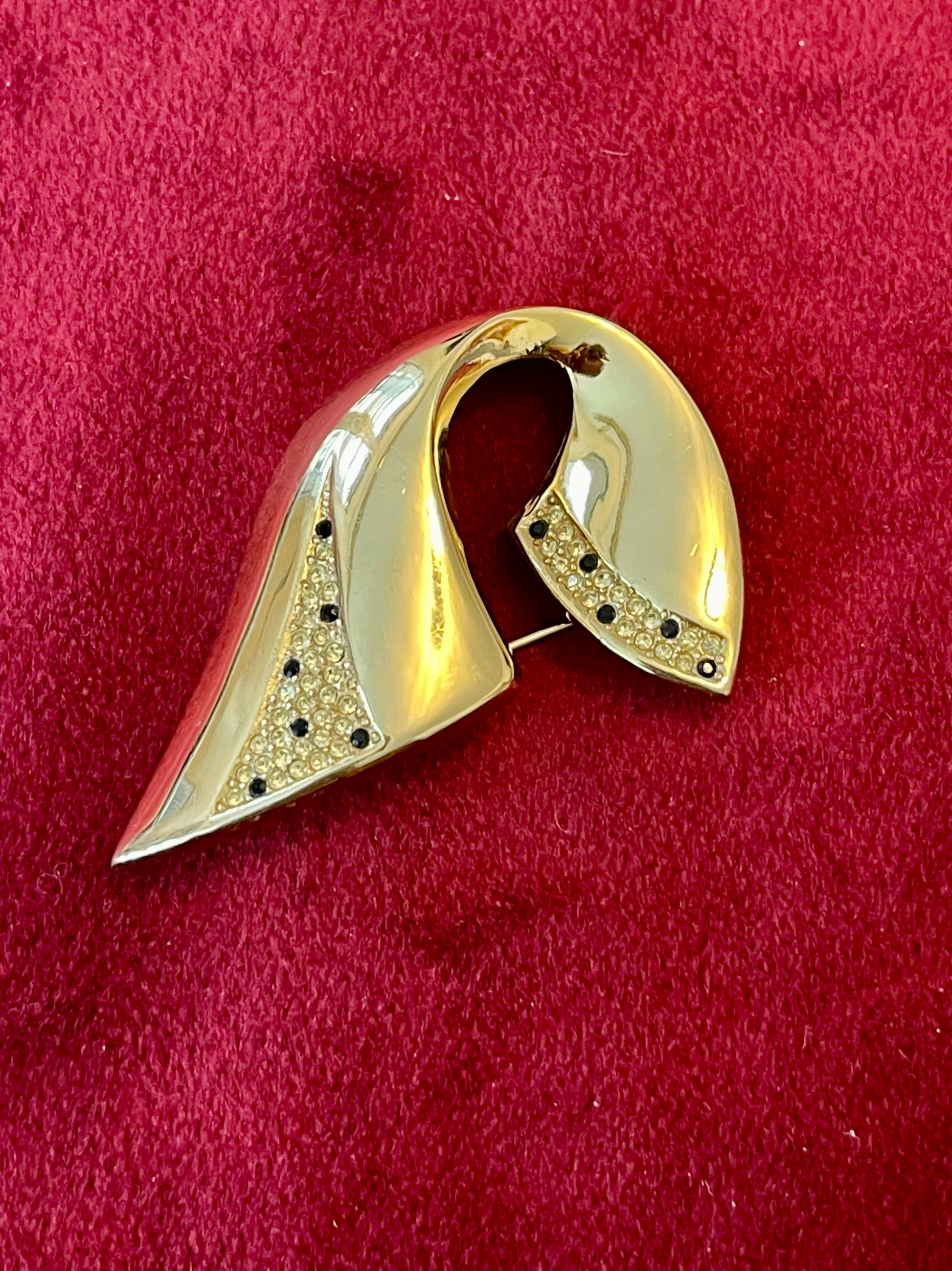 Vintage Christian Dior gold-tone sculptural brooch decorated with black and clear rhinestones, displayed against a red background