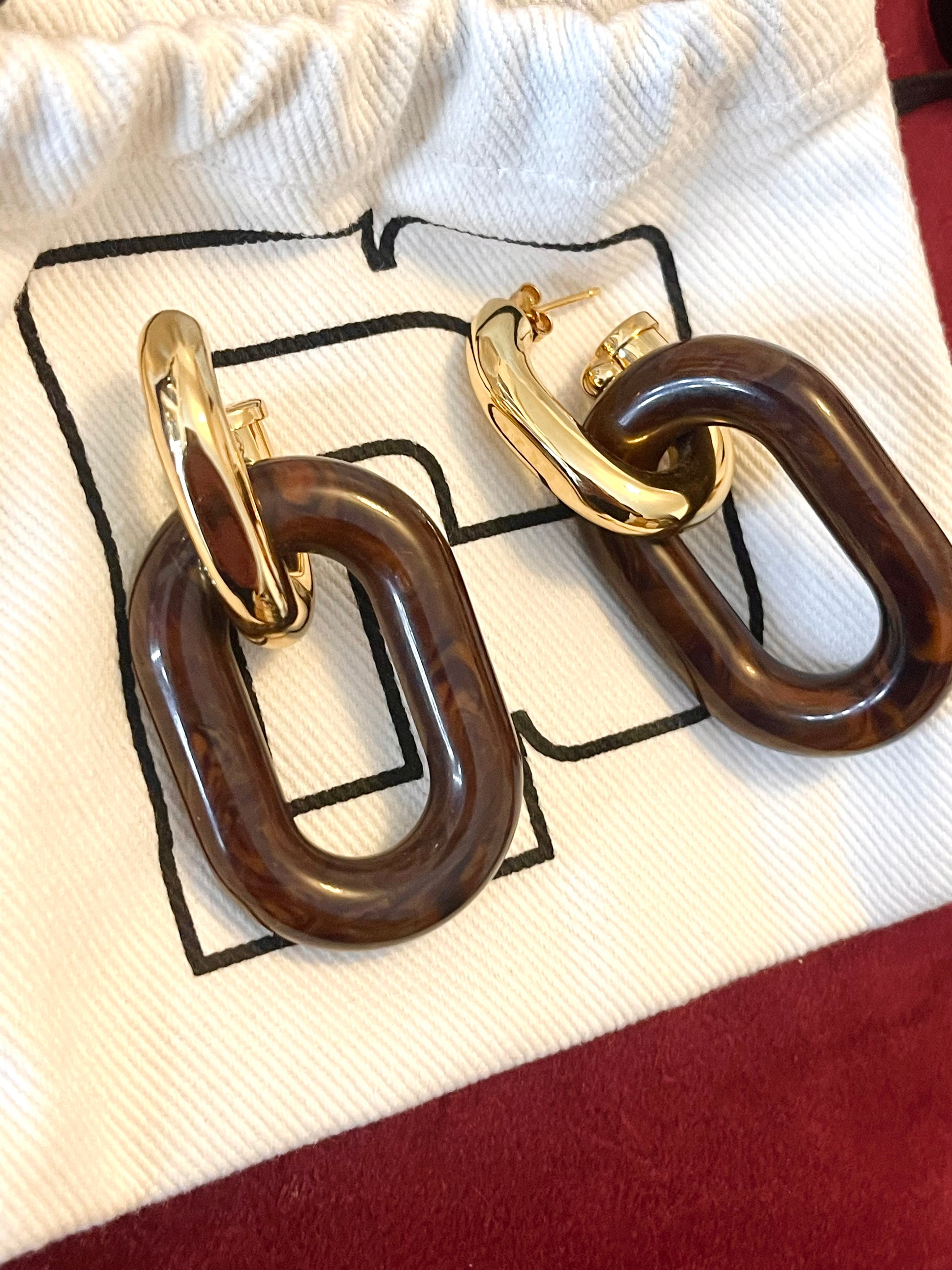 Paco Rabanne XL Link earrings in brown resin and gold metal, front view,Included pouch on red background 
