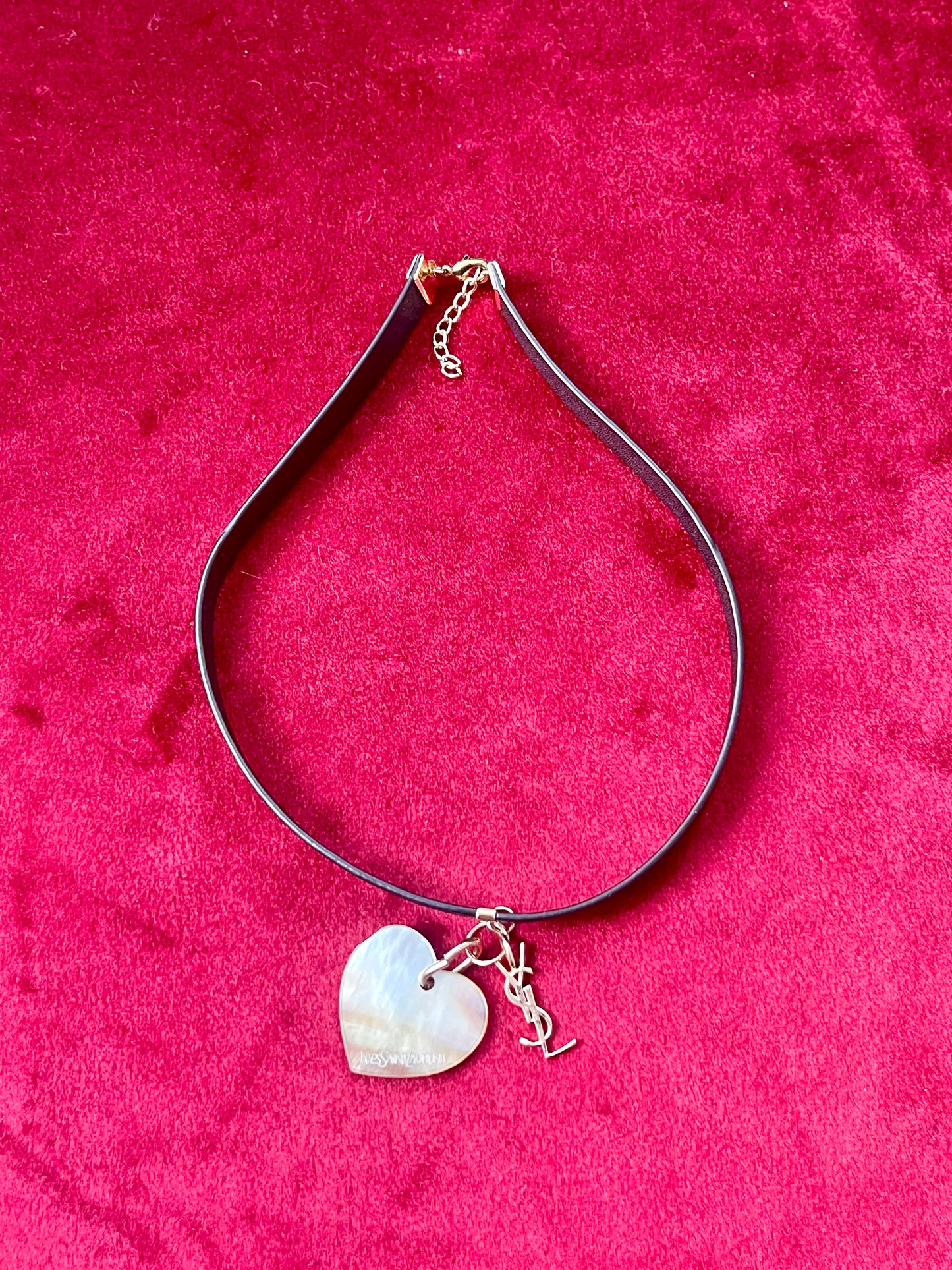 Yves Saint Laurent vintage heart seashell pendant YSL charm mounted on a black leather YSL Parfums necklace on a red velvet background 