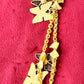 Detailed view of oxidation and patina on vintage Nina Ricci chain holding multiple YSL pendants on red velvet fabric.