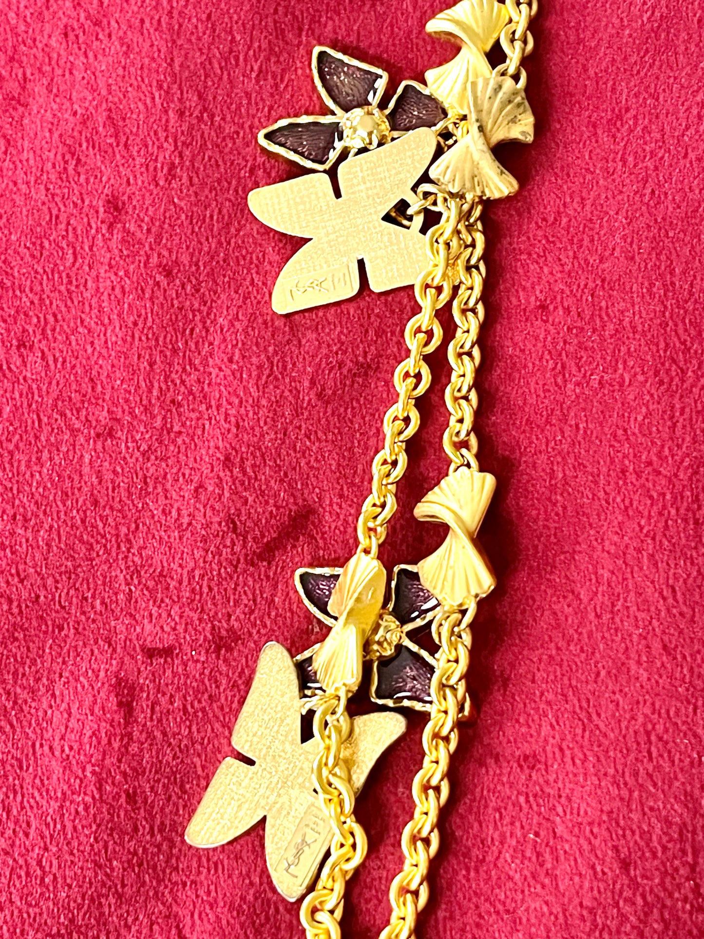 Detailed view of oxidation and patina on vintage Nina Ricci chain holding multiple YSL pendants on red velvet fabric.