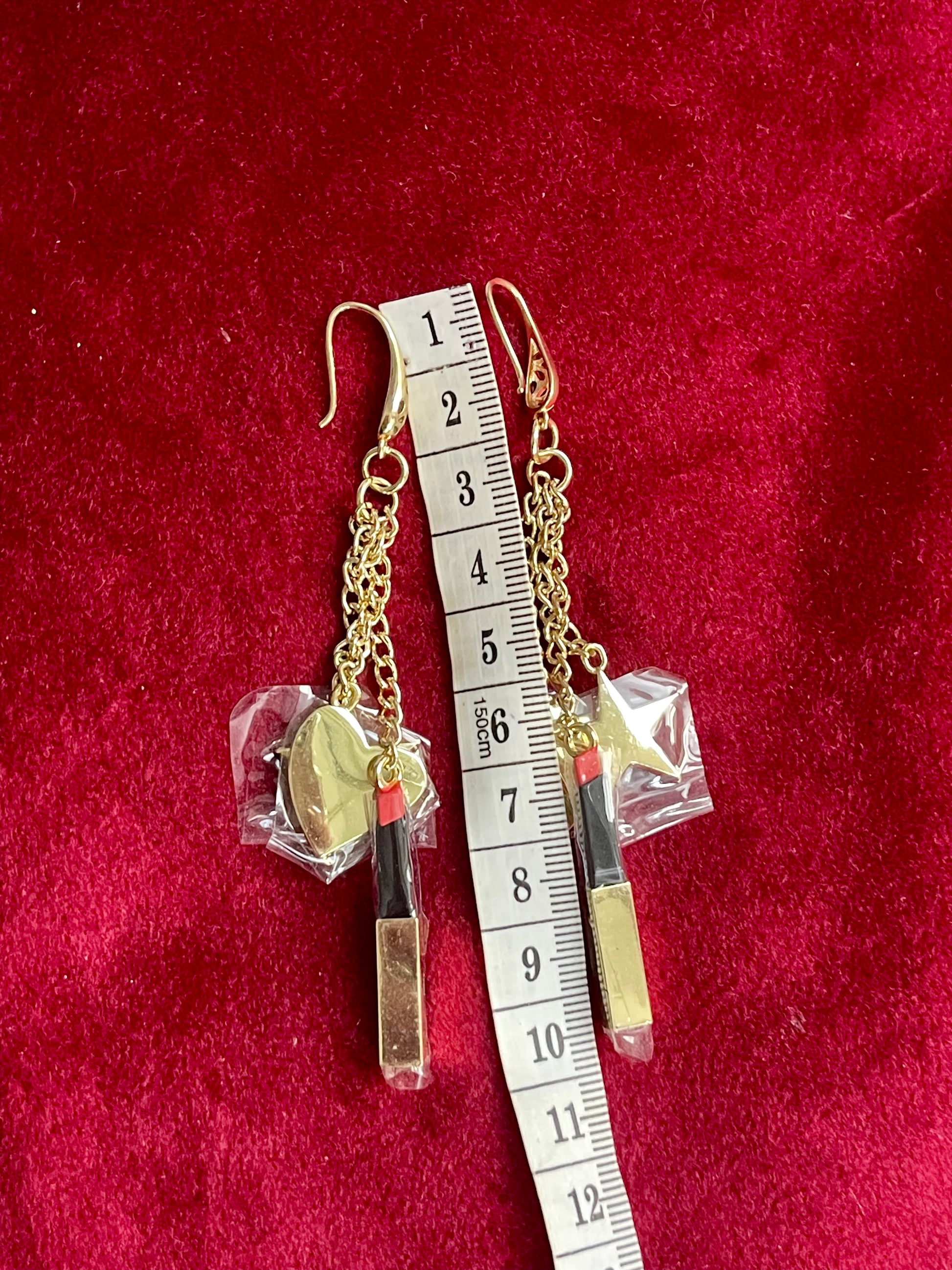 Earrings displayed together with a measuring tape showing asymmetrical design and charm arrangement
